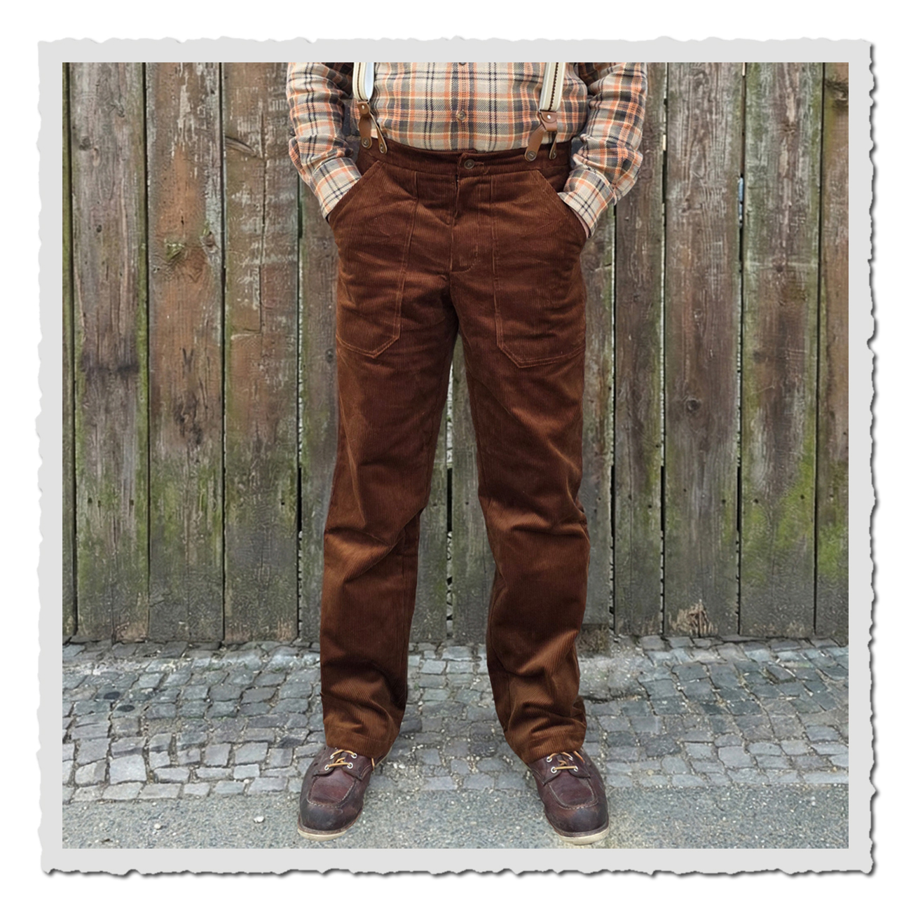 Retronia Arbeiterhose Gustav II in Braun, getragen mit Hosenträgern und Hemd, komplette Vorderansicht einer Person vor Holzzaun.